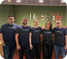 Cinco integrantes del equipo con camiseta de Smarteam frente al logo de HubSpot en sus oficinas.